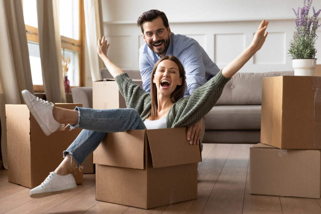 young bearded man in glasses pushing laughing wife in carton box